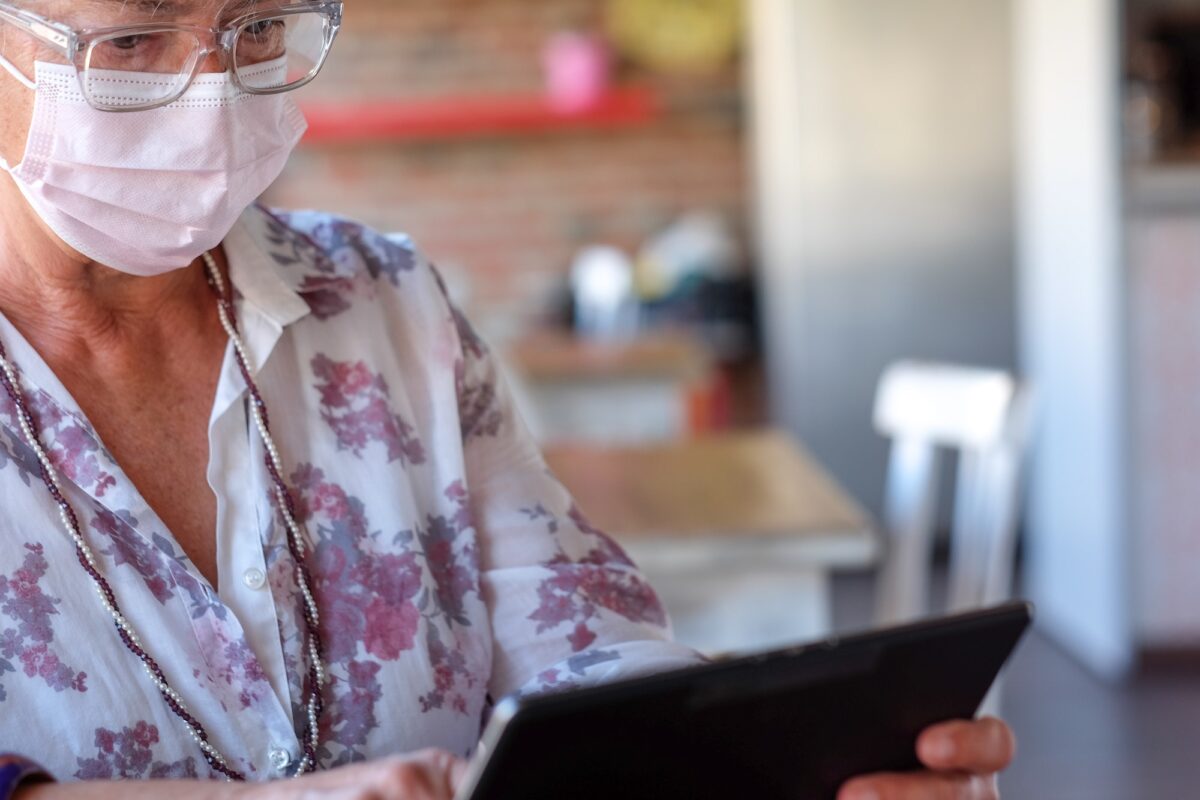 Mature woman with glasses working on digital tablet sitting at the coffee table