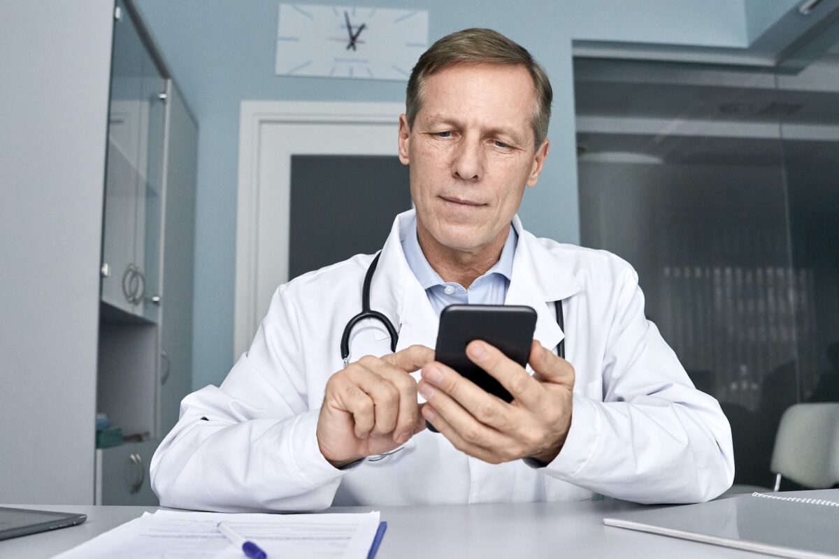 Old male doctor holding cellphone using mobile phone telemedicine technology.